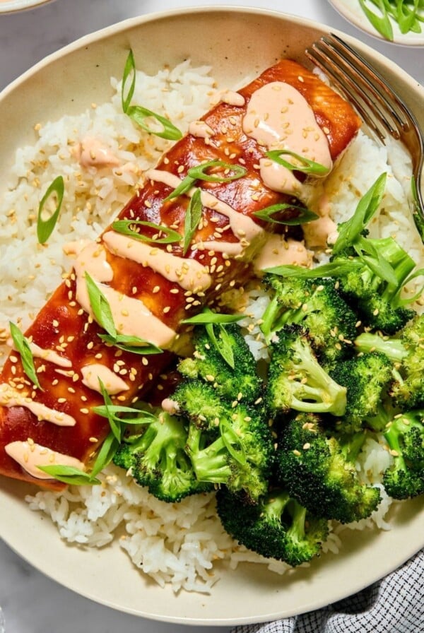 A plate filled with teriyaki salmon over rice and a side of broccoli.
