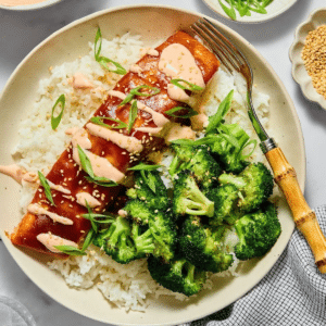 Baked teriyaki salmon with sauce on top on a plate with rice and broccoli.
