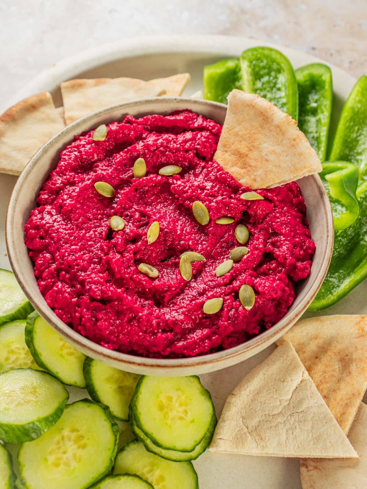 A bowl filled with beet hummus with pumpkin seeds on top.