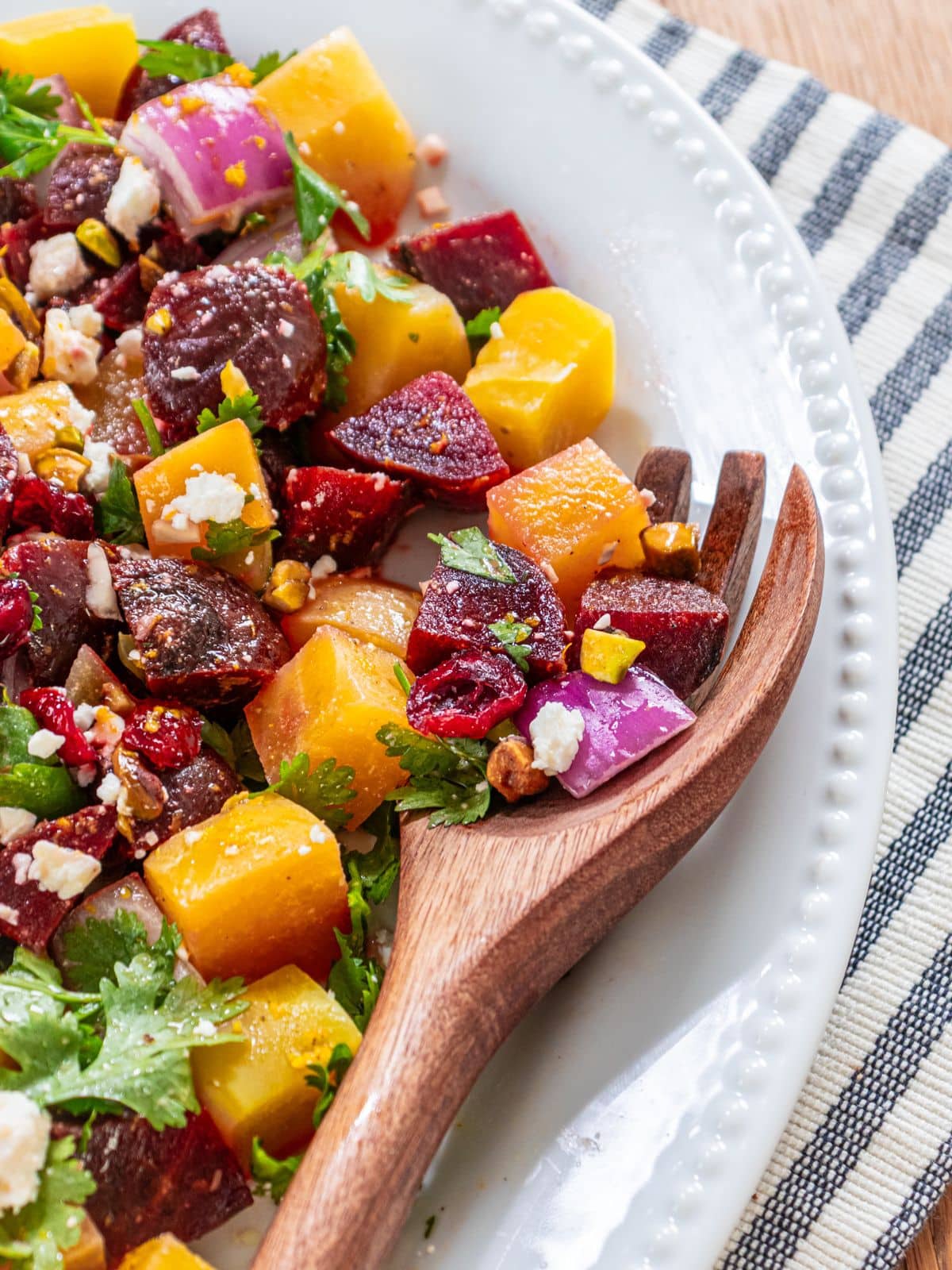 A wooden serving fork taking some beet salad from the dish.