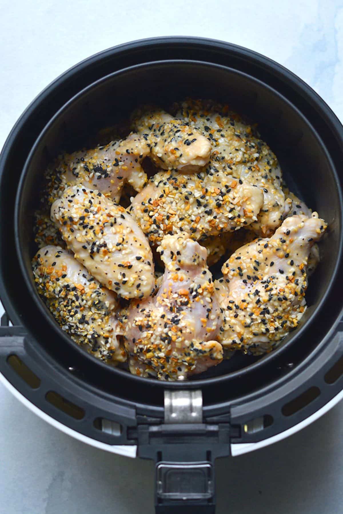 Wings with seasoning in an air fryer basket.