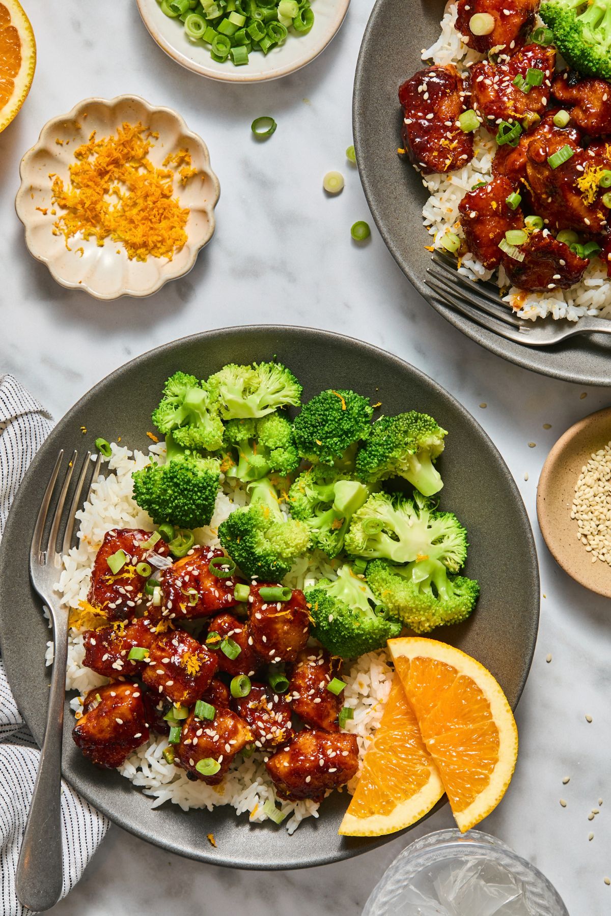 Healthy orange chicken over rice on a plate with broccoli and garnished with orange slices.