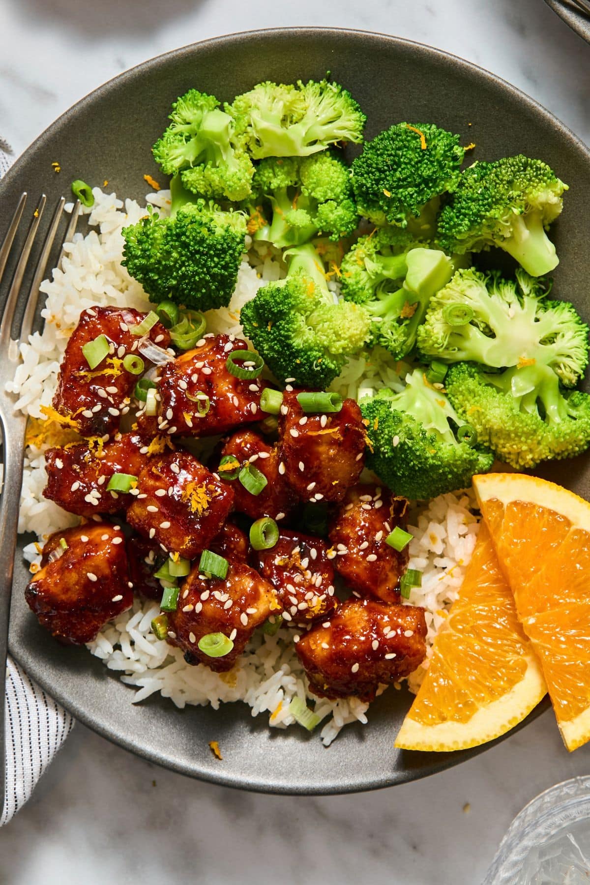 Healthy orange chicken over rice with a side of broccoli and a fork on the the side.