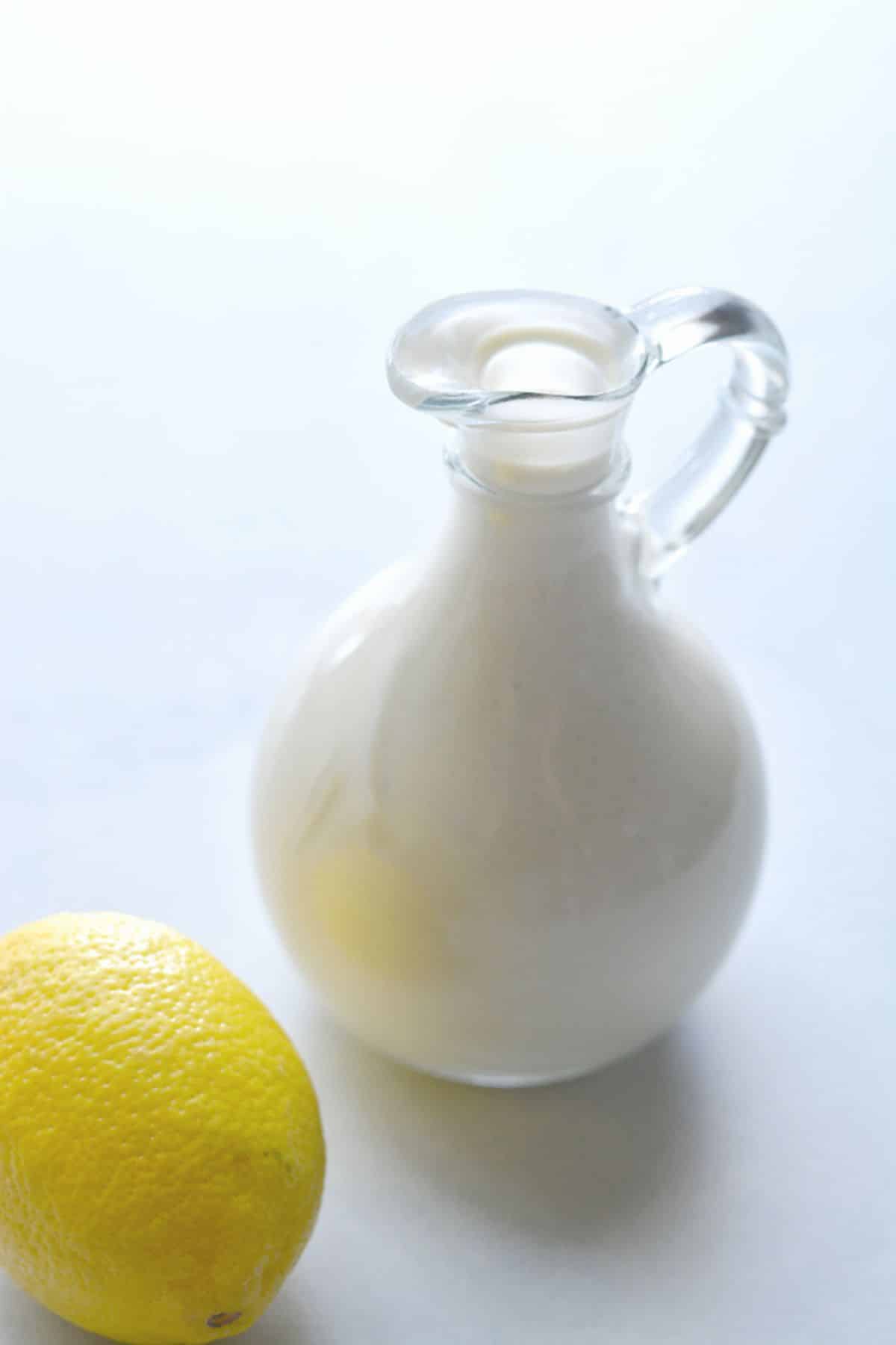 Low calorie caesar dressing in a glass pitcher with a lemon to the side.