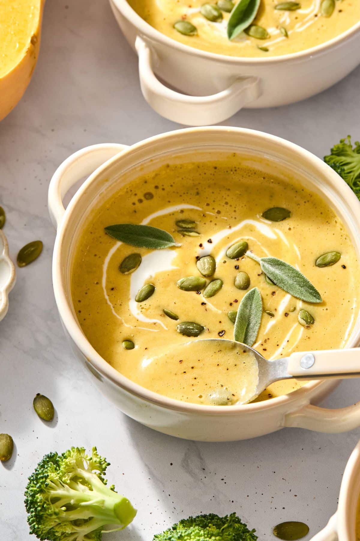 A spoon scooping out some soup with butternut squash broccoli.