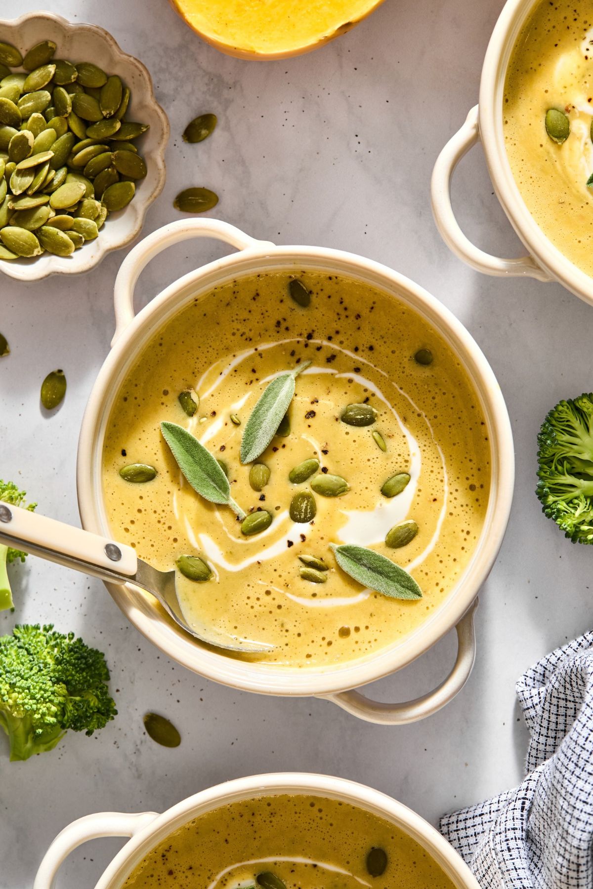A bowl with butternut squash soup with a spoon on the side and sage on top.