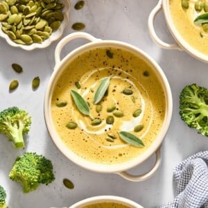 A bowl of butternut squash broccoli soup with seeds and sage on top.