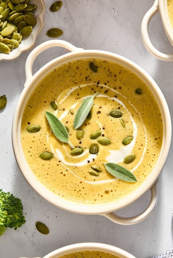 A bowl of butternut squash broccoli soup with seeds and sage on top.