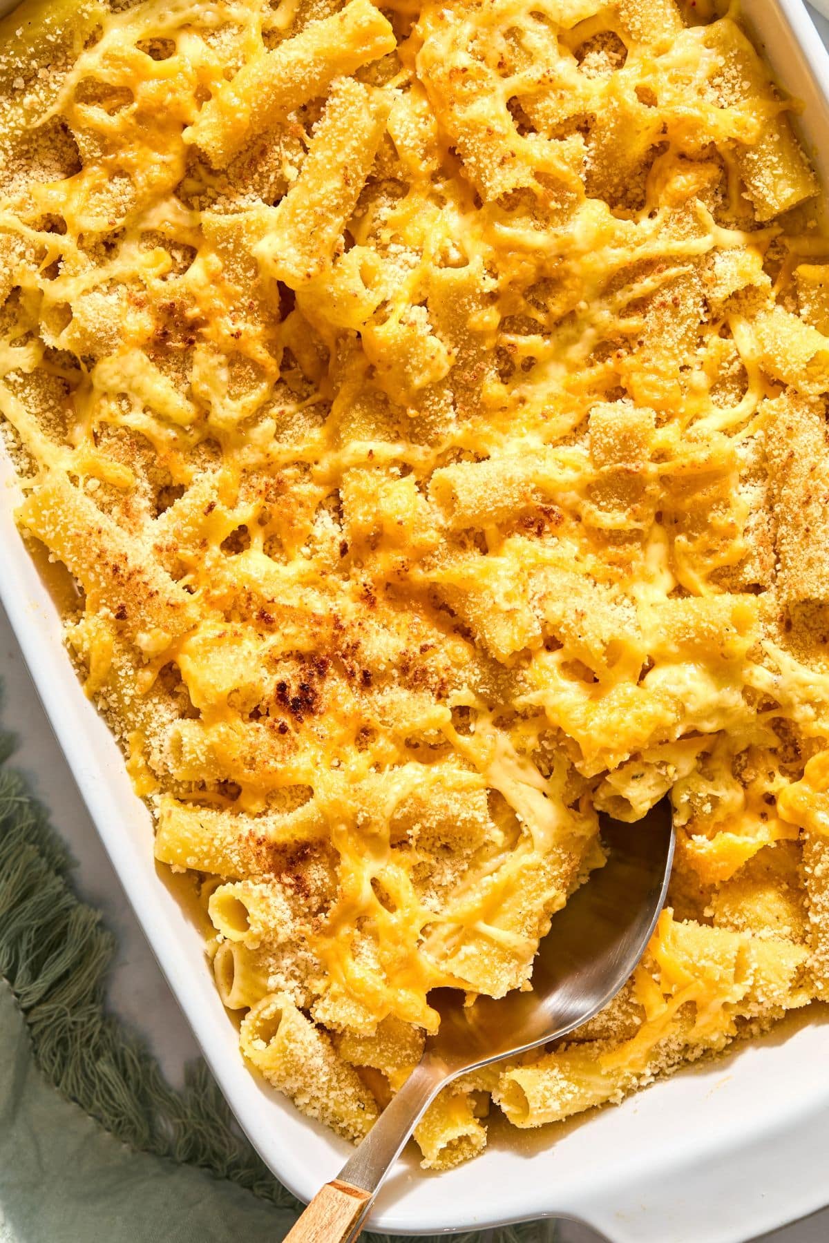 A casserole dish filled with mac and cheese with butternut squash and a spoon resting in the dish.