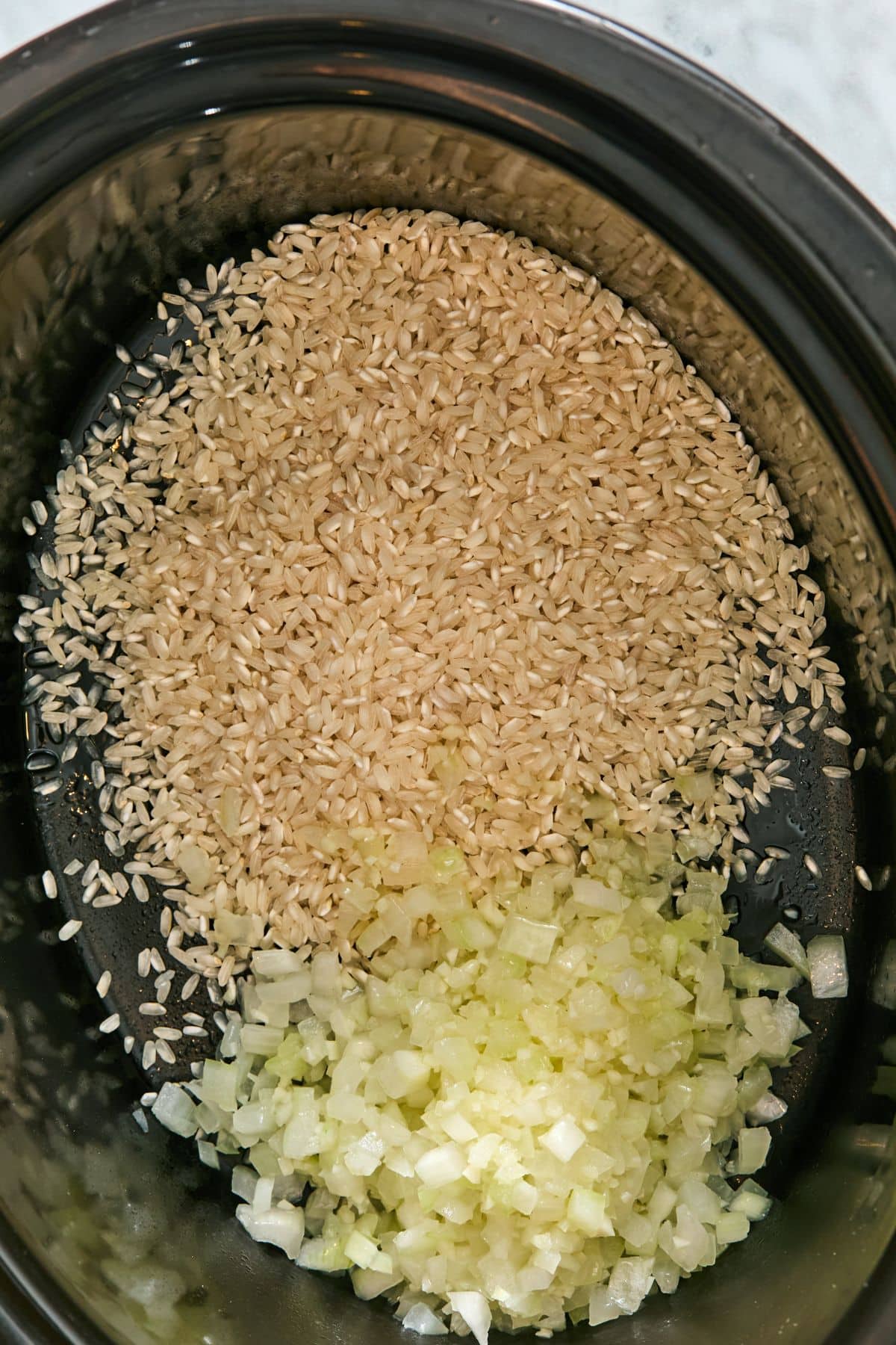 Rice, oil, onion and garlic added to a slow cooker.